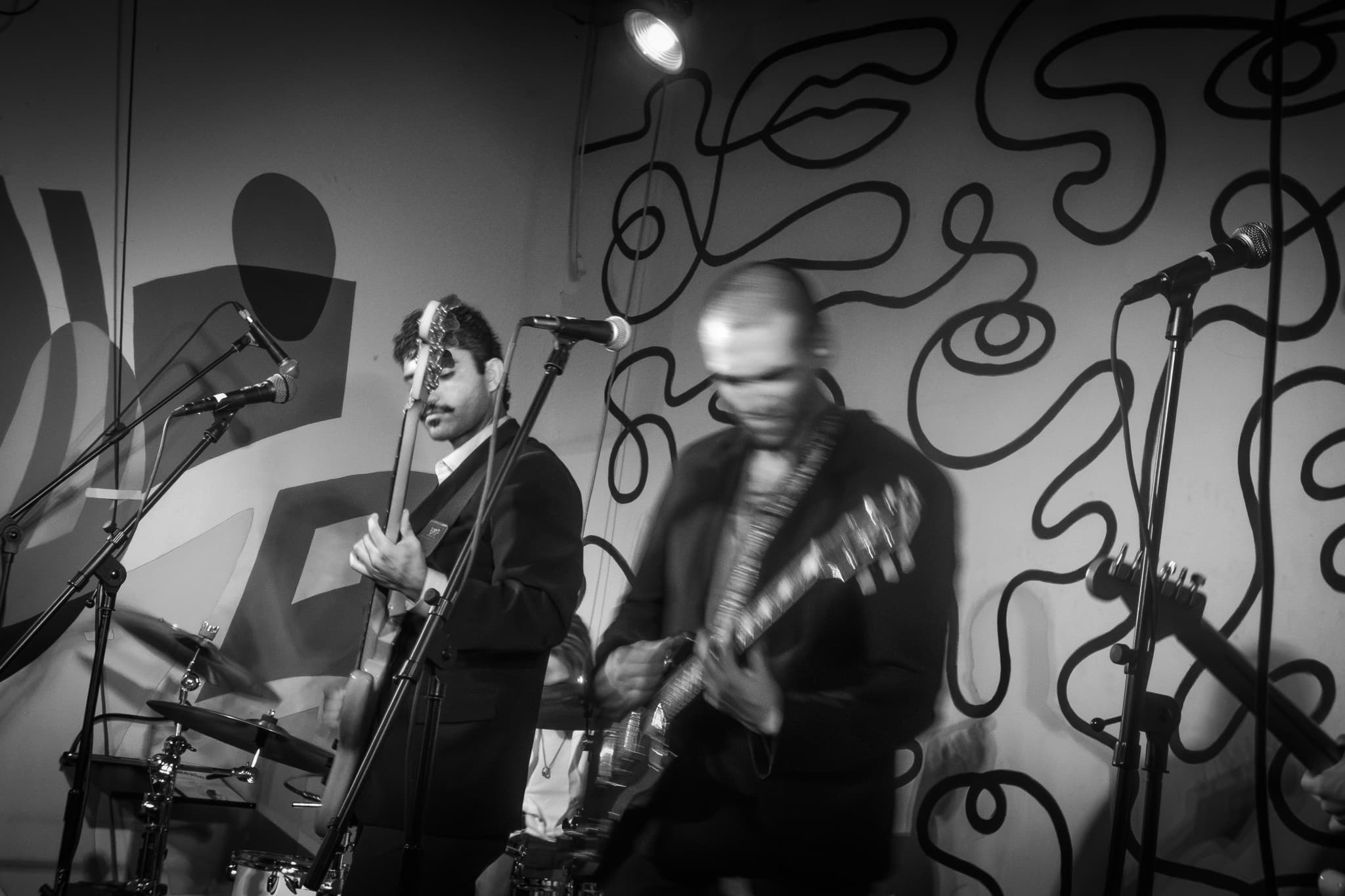 Dynamic motion blur cinematic black and white photography by Chase Tipton - Detailed shot of band passionately playing guitar, on a stage with dramatic lighting